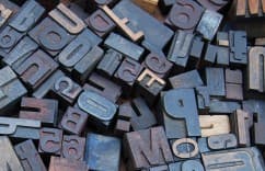 Pile of assorted letterpress blocks with letters and numbers in various shades of gray and brown.