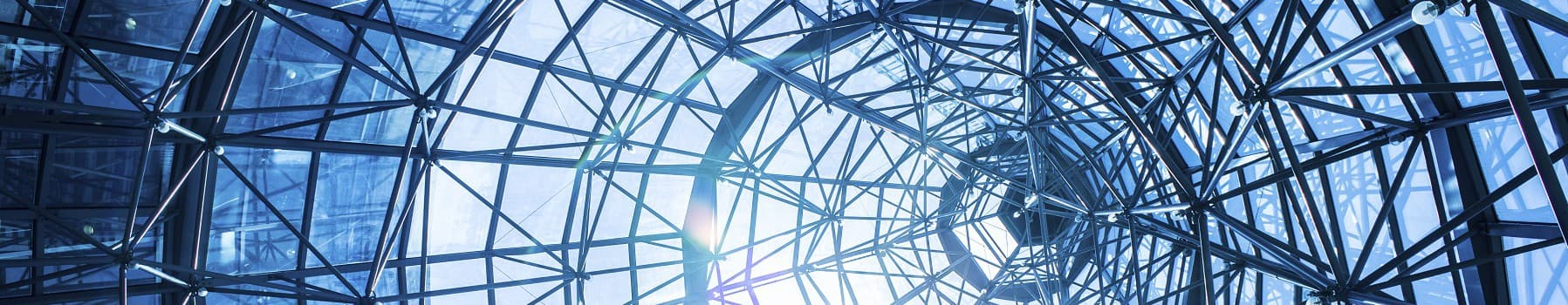Interior view of a glass dome structure with a steel framework and sunlight streaming through, against a blue sky, symbolizing modern architecture and transparency.