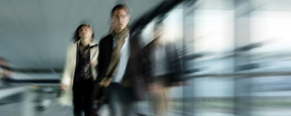 Blurred figures of people walking in a modern building with glass walls, captured in motion, symbolizing activity and progress.